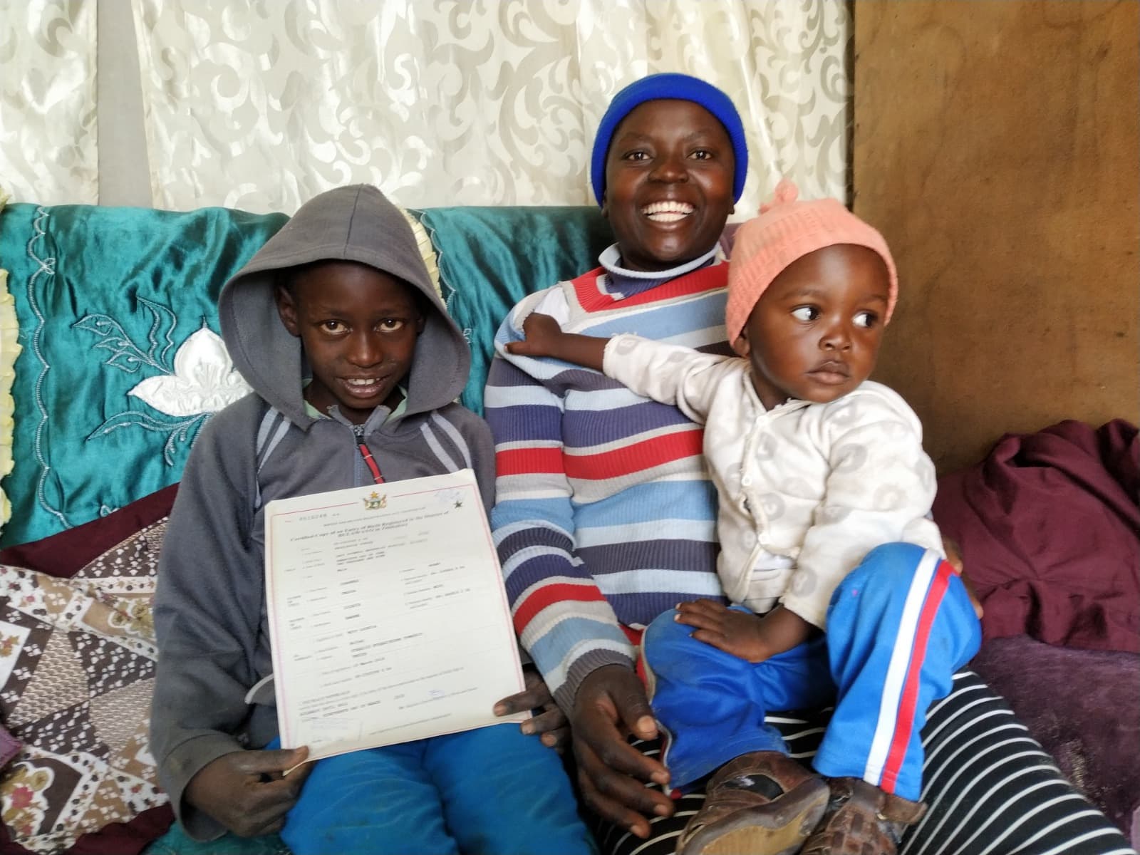 A mother and two children sitting together while the older boy holds a birth-registration document.