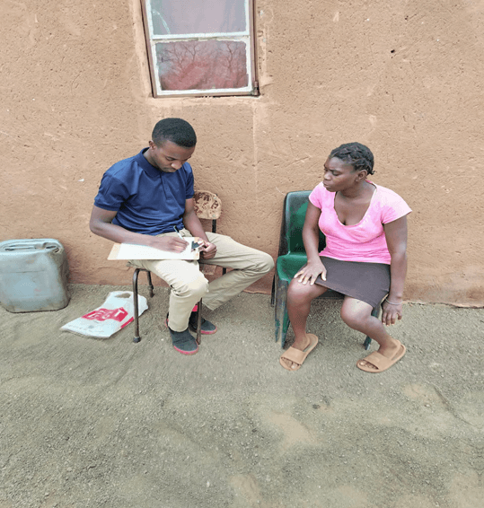 Trinity Project officer with Portia during a home visit, taking notes outside her home.